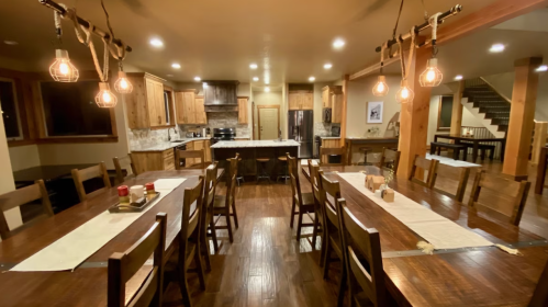 A spacious dining area with wooden tables and chairs, warm lighting, and a modern kitchen in the background.